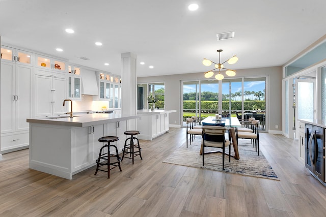 kitchen with pendant lighting, sink, wine cooler, white cabinets, and a center island with sink