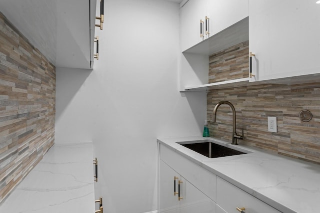 kitchen with light stone counters, white cabinetry, and sink