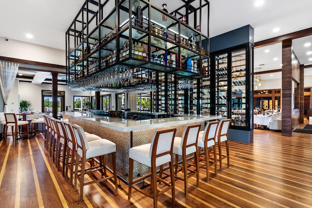 bar with decorative columns, a towering ceiling, and hardwood / wood-style floors