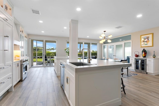 kitchen with sink, white cabinetry, hanging light fixtures, beverage cooler, and a kitchen island with sink