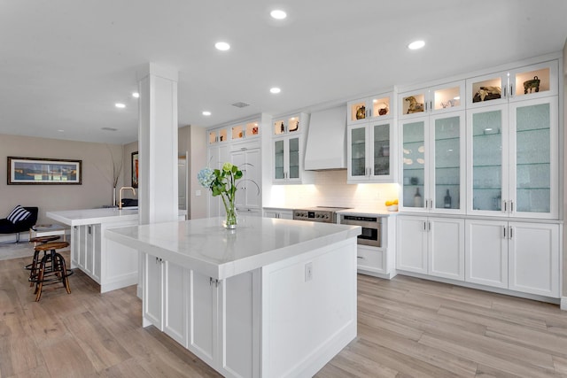 kitchen featuring white cabinetry, light stone countertops, a kitchen island with sink, and custom range hood