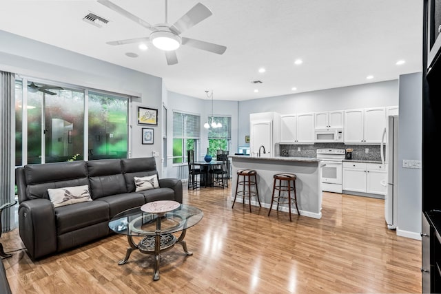 living room featuring ceiling fan with notable chandelier, light hardwood / wood-style flooring, and sink