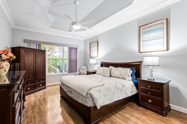 bedroom with ceiling fan, a raised ceiling, crown molding, a textured ceiling, and light wood-type flooring