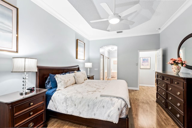 bedroom featuring ceiling fan, light hardwood / wood-style floors, ornamental molding, and a textured ceiling