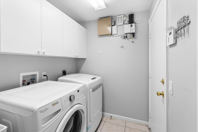 laundry room featuring cabinets, light tile patterned floors, a textured ceiling, and washing machine and clothes dryer