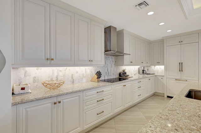 kitchen featuring black electric stovetop, wall chimney exhaust hood, white cabinets, and light stone countertops