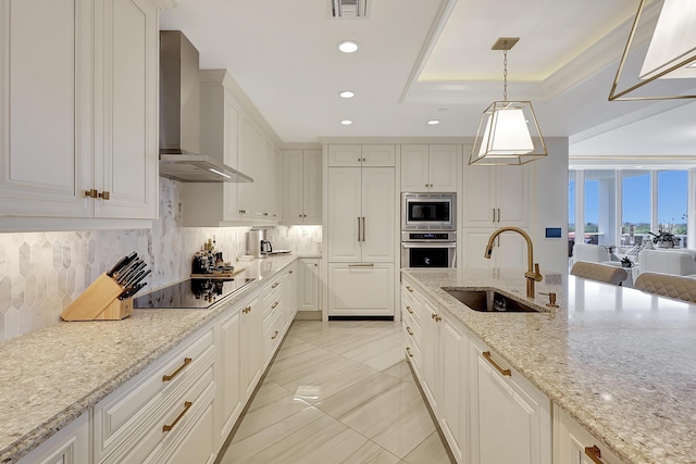 kitchen with wall chimney range hood, sink, hanging light fixtures, light stone countertops, and appliances with stainless steel finishes