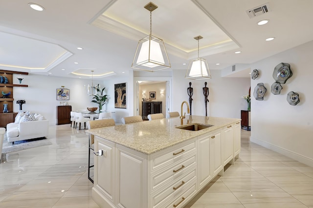 kitchen with a center island with sink, sink, hanging light fixtures, and a tray ceiling