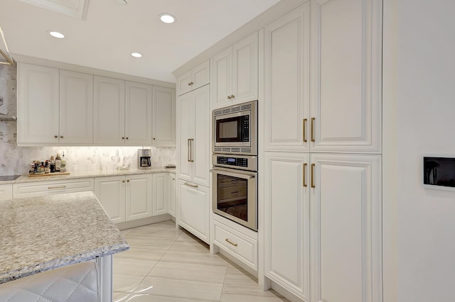 kitchen featuring decorative backsplash, appliances with stainless steel finishes, light stone counters, light tile patterned floors, and white cabinets