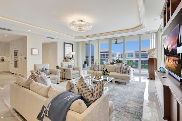 living room with ceiling fan with notable chandelier, a raised ceiling, and a wall of windows