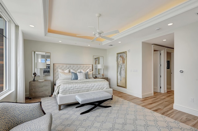 bedroom featuring ceiling fan, ornamental molding, light hardwood / wood-style flooring, and a tray ceiling