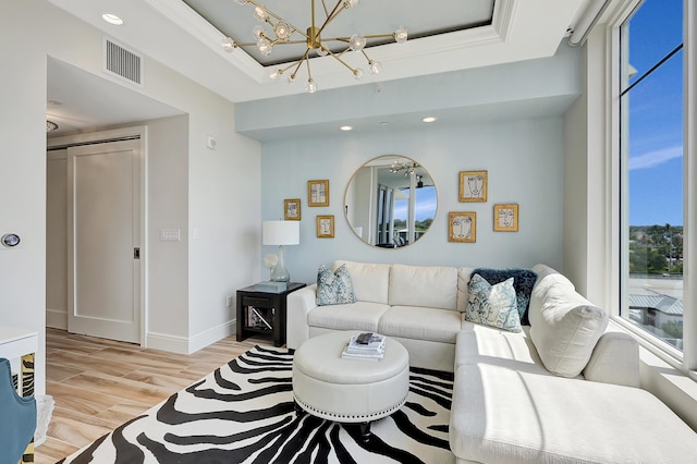 living room with light wood-type flooring, an inviting chandelier, a raised ceiling, and crown molding