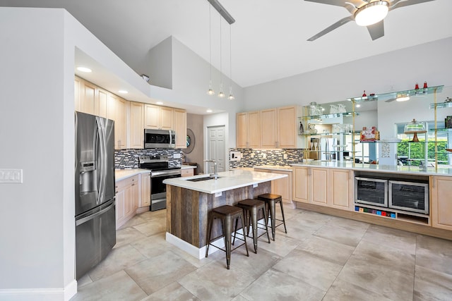 kitchen with light brown cabinets, a center island with sink, a kitchen breakfast bar, sink, and stainless steel appliances