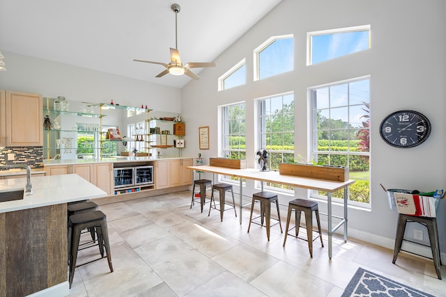 tiled dining room featuring ceiling fan, beverage cooler, sink, and high vaulted ceiling