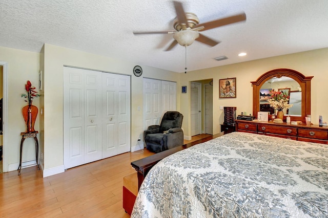 bedroom featuring two closets, a textured ceiling, light hardwood / wood-style floors, and ceiling fan