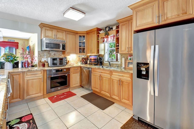 kitchen featuring light stone counters, sink, stainless steel appliances, and light tile patterned flooring