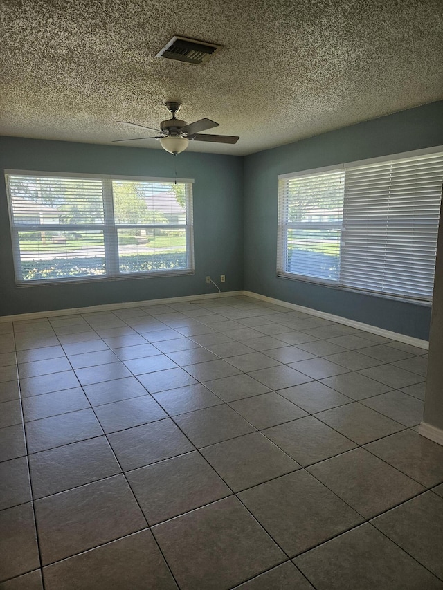 tiled empty room featuring plenty of natural light, ceiling fan, and a textured ceiling