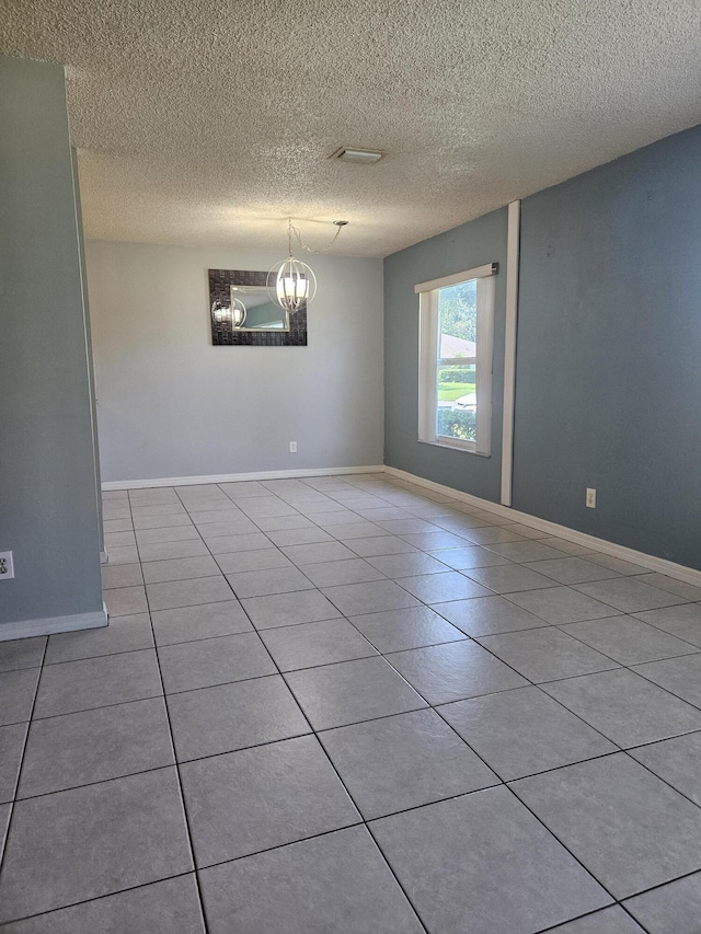 spare room featuring a notable chandelier, light tile patterned flooring, and a textured ceiling