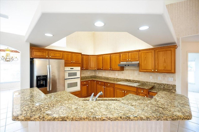 kitchen featuring kitchen peninsula, light stone countertops, white appliances, sink, and light tile patterned flooring