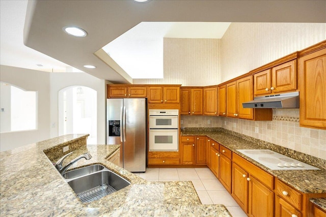 kitchen featuring backsplash, light stone counters, white appliances, sink, and light tile patterned floors