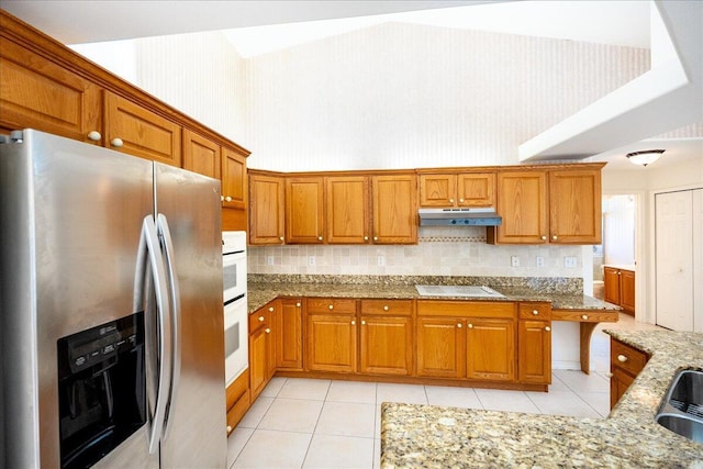 kitchen with light stone countertops, decorative backsplash, white appliances, sink, and light tile patterned floors