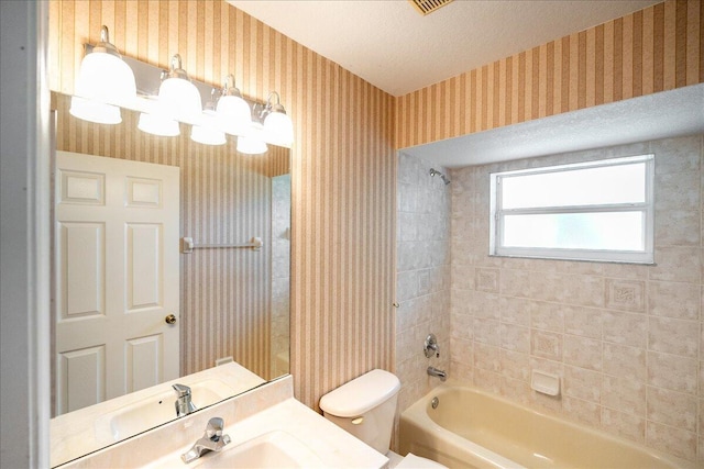 full bathroom with a textured ceiling, vanity, tiled shower / bath combo, and toilet