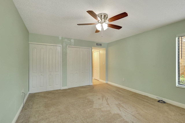 unfurnished bedroom featuring light carpet, two closets, a textured ceiling, and ceiling fan