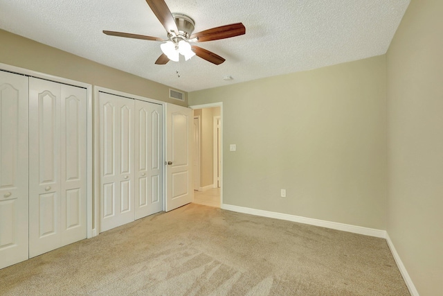 unfurnished bedroom featuring two closets, light colored carpet, a textured ceiling, and ceiling fan