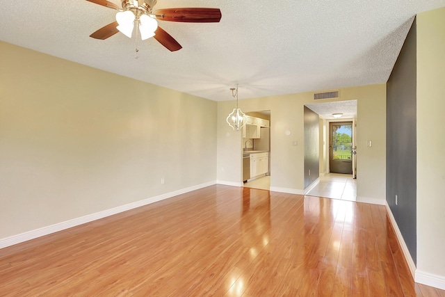 unfurnished room with ceiling fan with notable chandelier, sink, a textured ceiling, and light wood-type flooring