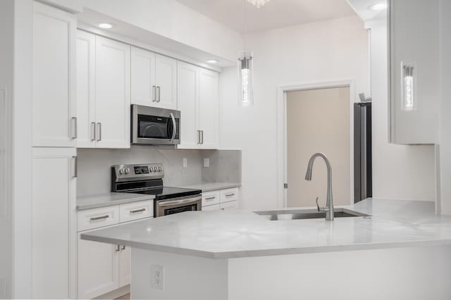 kitchen featuring kitchen peninsula, stainless steel appliances, sink, decorative light fixtures, and white cabinetry