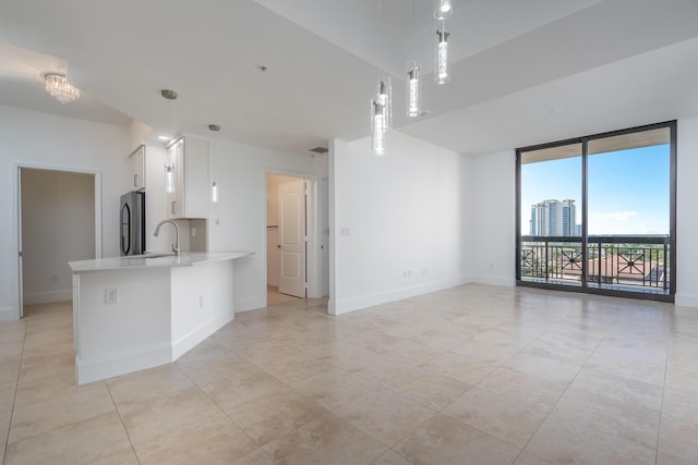 kitchen with white cabinets, hanging light fixtures, light tile patterned floors, kitchen peninsula, and stainless steel refrigerator