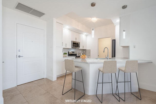 kitchen with kitchen peninsula, a breakfast bar, stainless steel appliances, sink, and white cabinetry