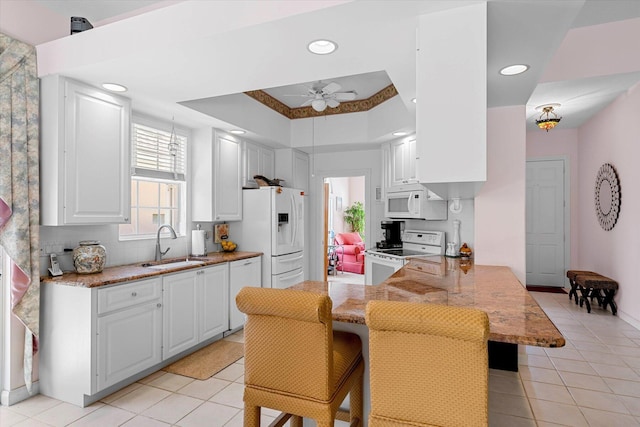 kitchen featuring white appliances, white cabinets, sink, a tray ceiling, and kitchen peninsula