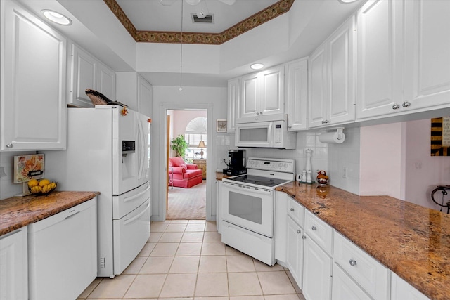 kitchen with white cabinetry, light tile patterned floors, dark stone counters, and white appliances