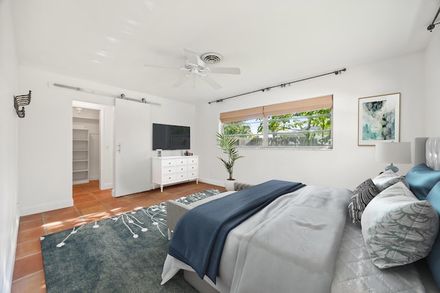 bedroom with tile patterned flooring, ceiling fan, a barn door, a spacious closet, and a closet