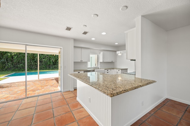 kitchen featuring white cabinets, light stone counters, kitchen peninsula, a textured ceiling, and light tile patterned floors