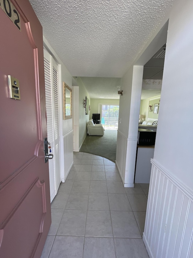 hall with a textured ceiling and light tile patterned floors