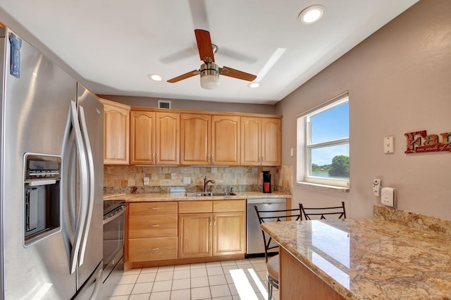 kitchen featuring light stone countertops, decorative backsplash, stainless steel appliances, sink, and light tile patterned floors