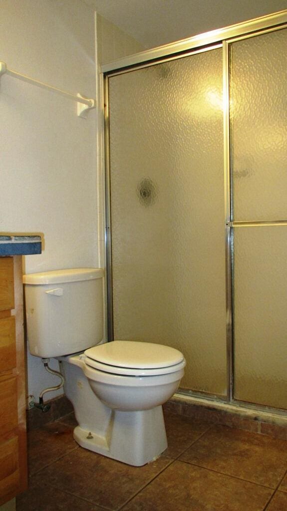 bathroom with tile patterned floors, toilet, and a shower with shower door