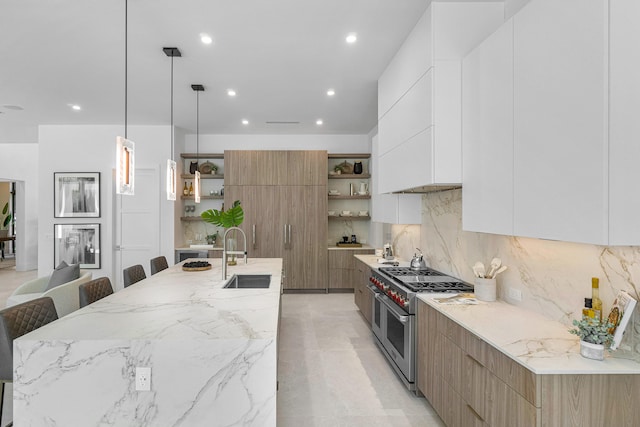 kitchen featuring sink, double oven range, white cabinetry, and an island with sink