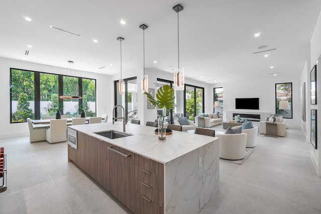 kitchen featuring light stone countertops, decorative light fixtures, a large island with sink, light tile floors, and sink