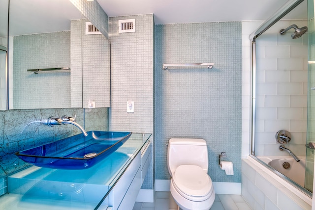 full bathroom featuring tile patterned flooring, toilet, shower / bath combination with glass door, vanity, and tile walls