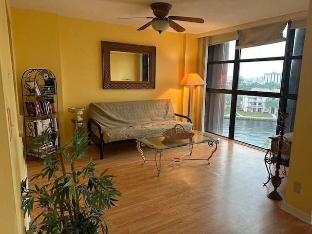 living room with wood-type flooring, a water view, ceiling fan, and a wall of windows