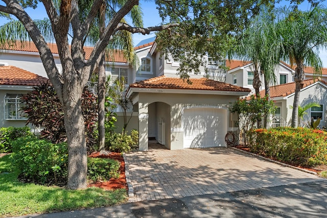 mediterranean / spanish home with a garage, decorative driveway, a tile roof, and stucco siding