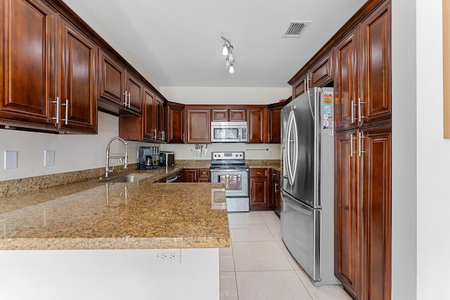 kitchen with light tile patterned floors, a textured ceiling, light stone counters, stainless steel appliances, and a sink