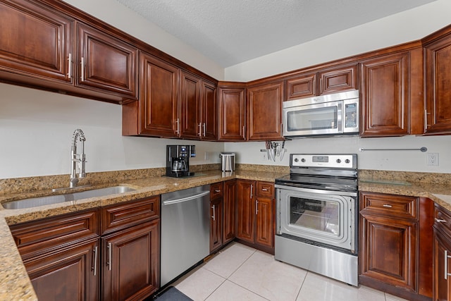 kitchen with light tile patterned floors, a textured ceiling, stainless steel appliances, a sink, and light stone countertops