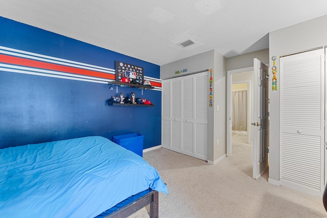 carpeted bedroom with visible vents, a textured ceiling, baseboards, and two closets