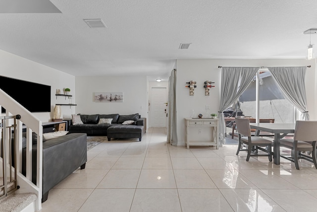 living room featuring stairway, light tile patterned flooring, visible vents, and a textured ceiling