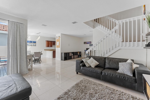 living room featuring light tile patterned floors, visible vents, a textured ceiling, and stairs