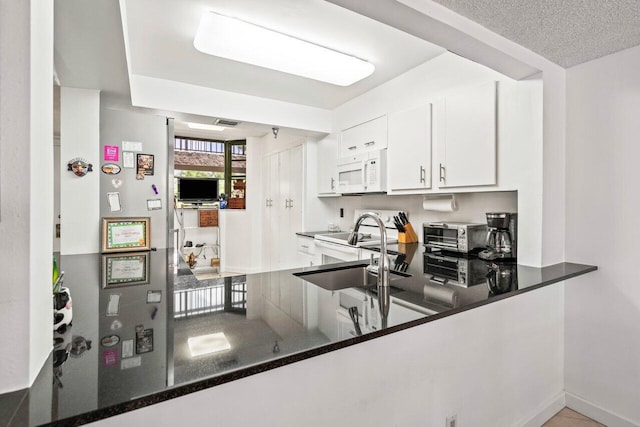 kitchen featuring white appliances, dark stone countertops, a textured ceiling, sink, and white cabinets